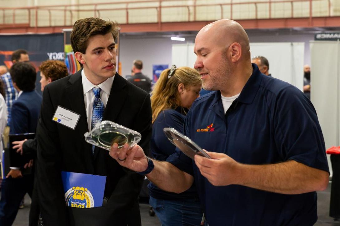 A recruiter at Kettering's Co-Op Fair talks to a Kettering student and shows off his company's products